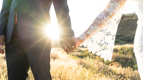 A man and a woman just married hold hands outdoors.