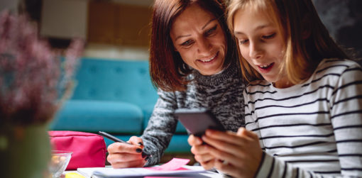 A woman and her daughter use a smartphone, a notebook, and sticky notes to discuss money and personal values.