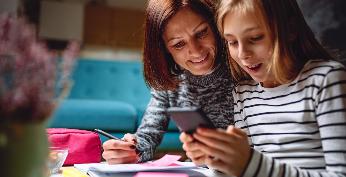 A woman and her daughter use a smartphone, a notebook, and sticky notes to discuss money and personal values.