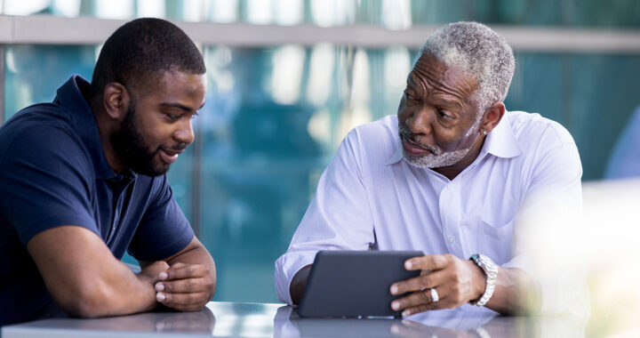 Two men, father and son, discuss something they are viewing online.