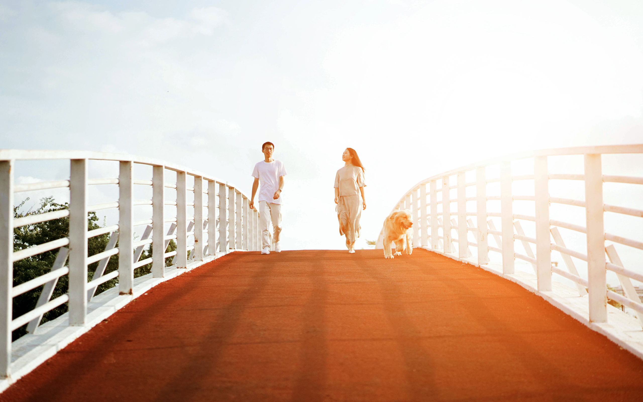 Man and woman walking dog across a bridge