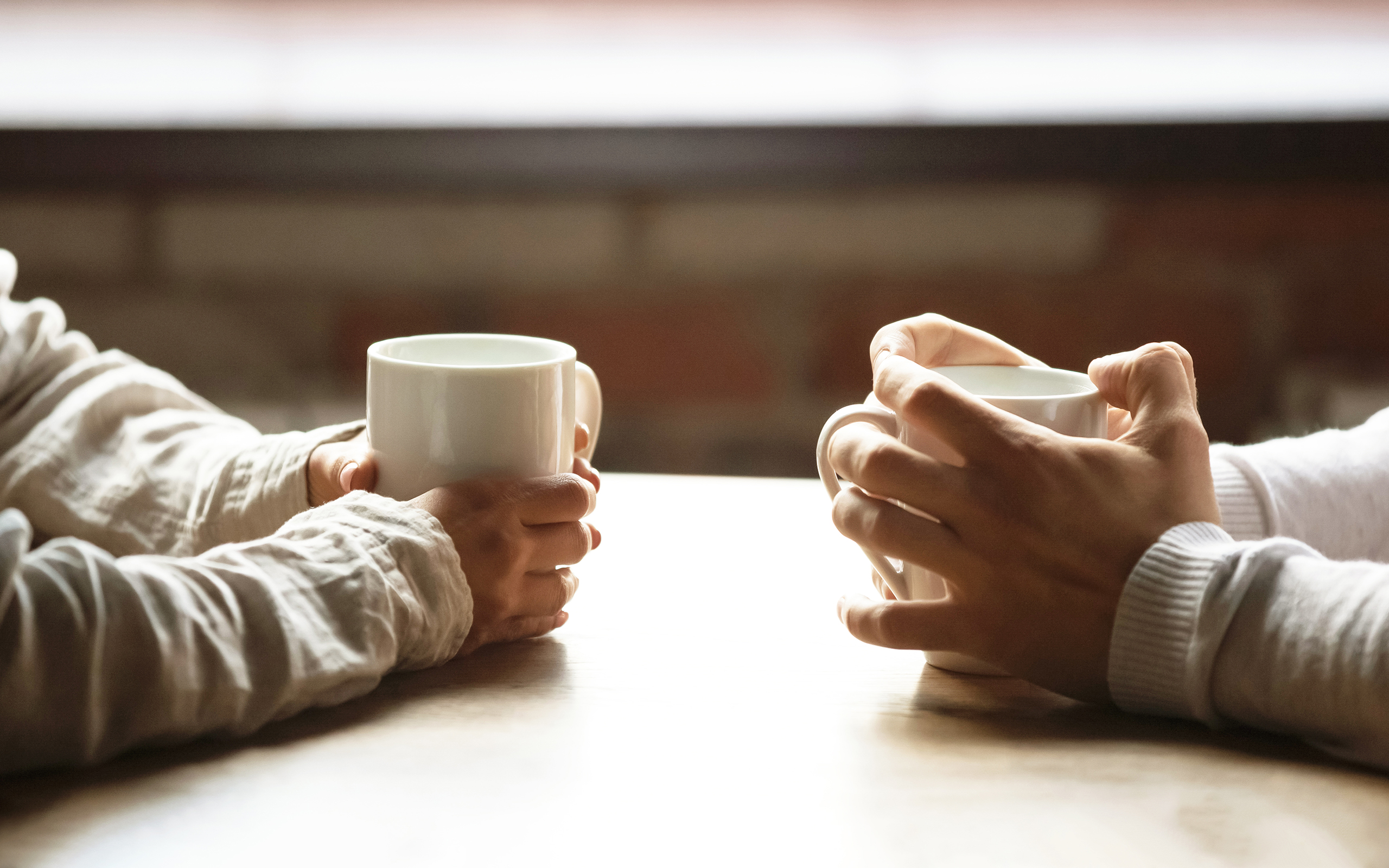 The hands of two people sitting opposite each other holding mugs