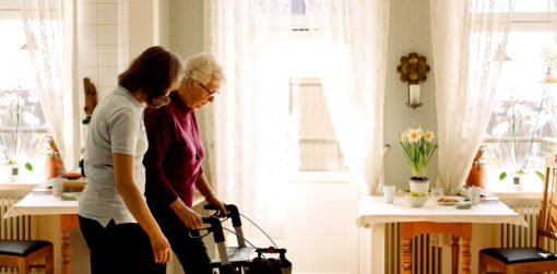an aide walks alongside an elderly woman using an upright walker