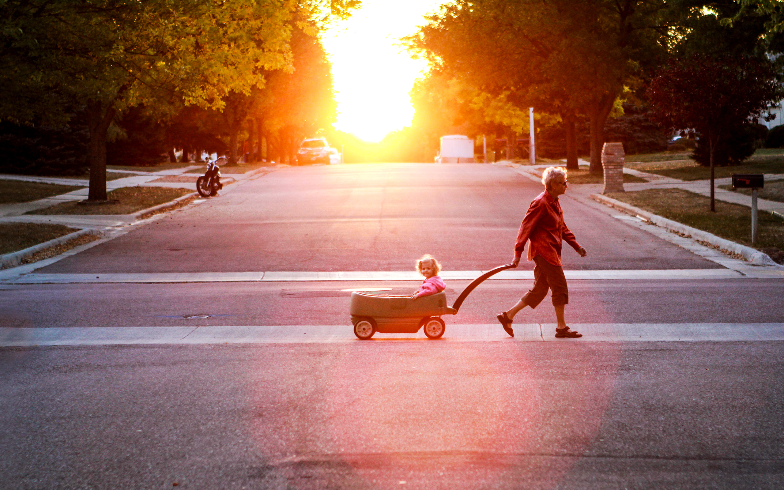 A grandparent pulls a young child in a wagon across the street