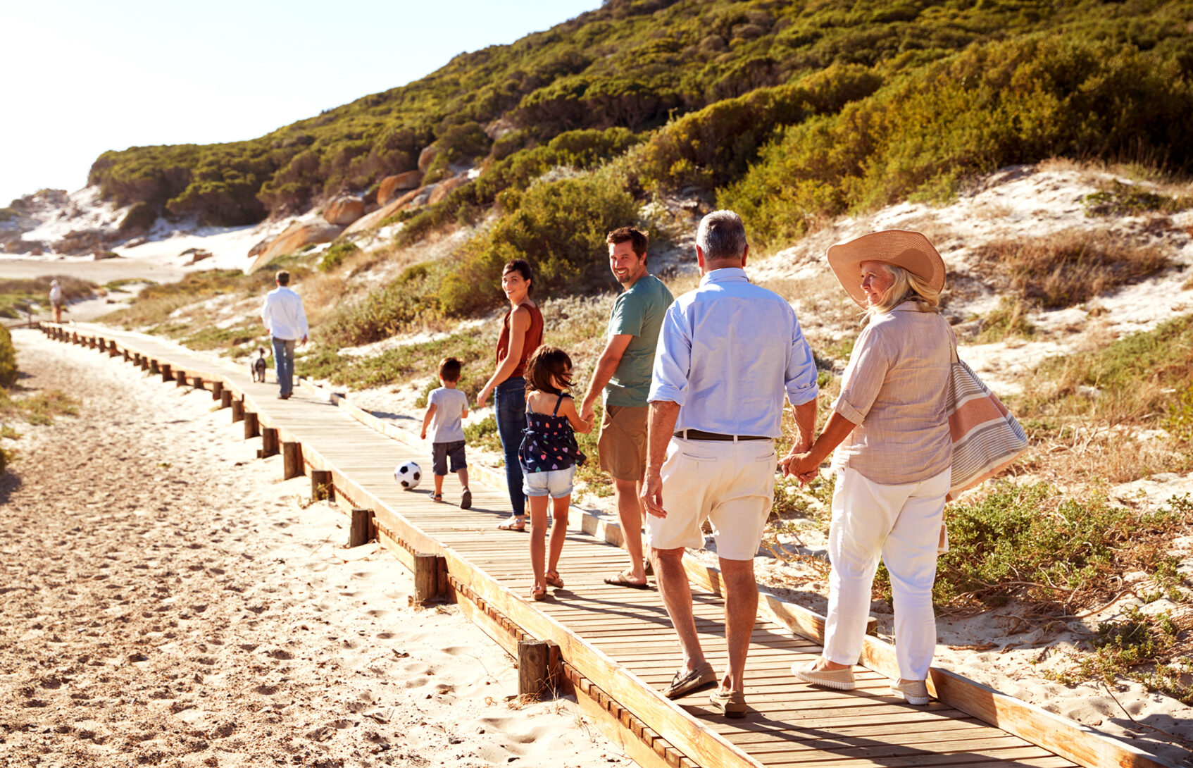 A multigenerational family walks along a wooden path on the beach