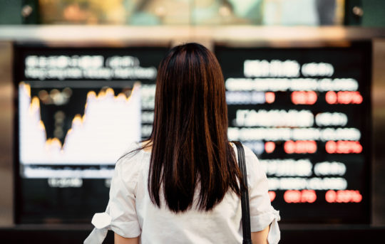 A woman looks at a stock market display board.