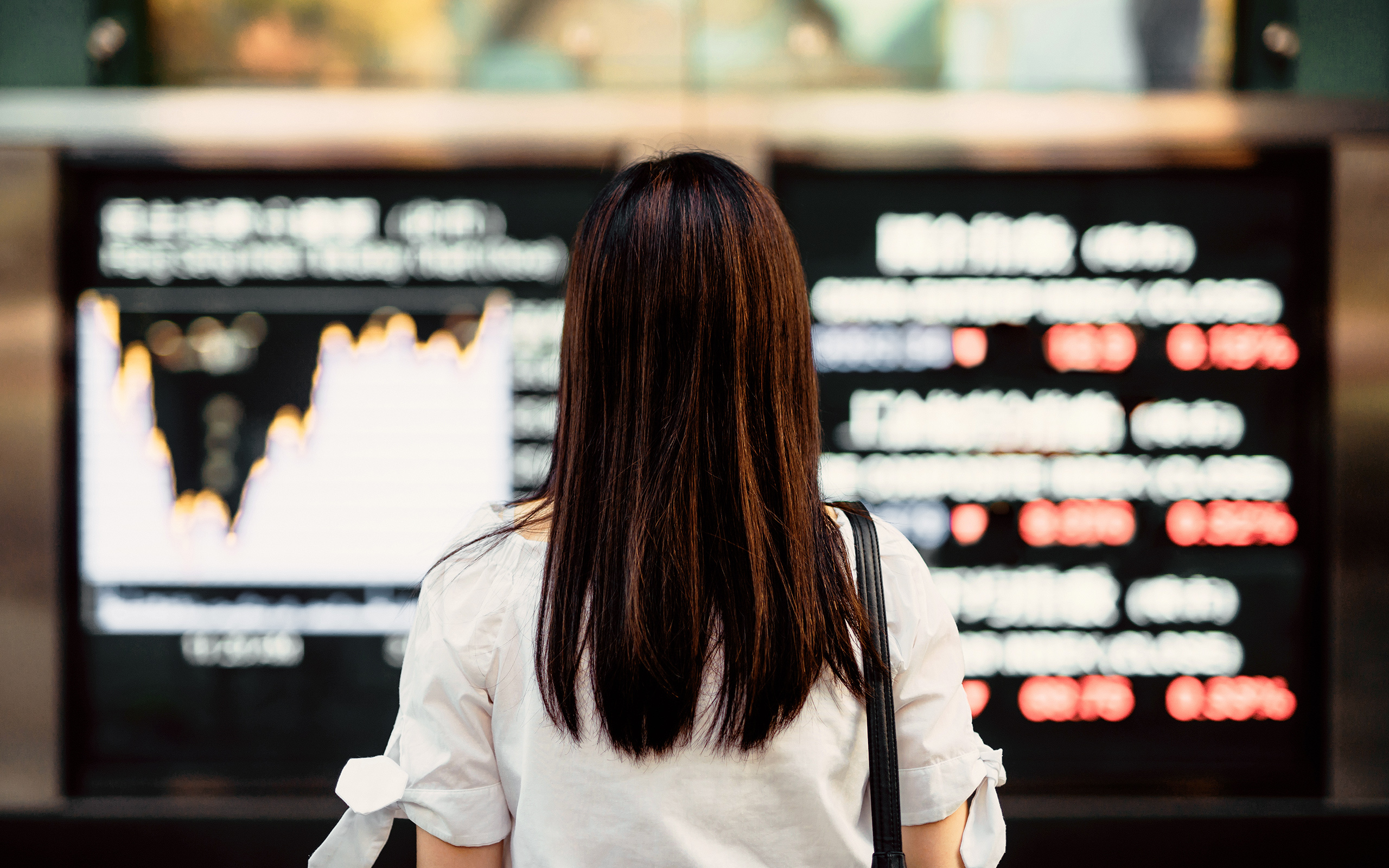 A woman looks at a stock market display board.