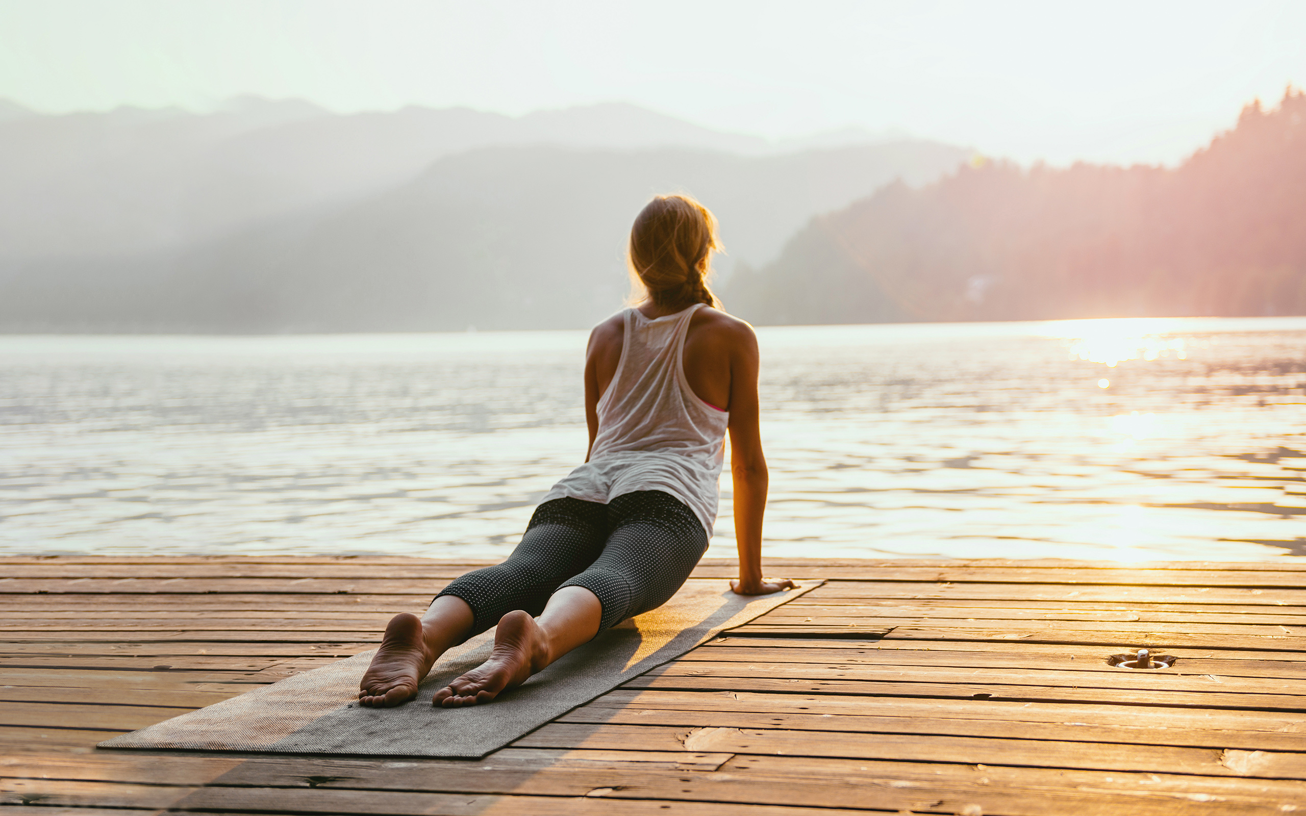 A woman stretching on a yoga mat on a dock looking out over the water.