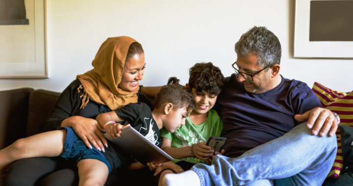A couple smiles and reads with their grandchildren on a couch