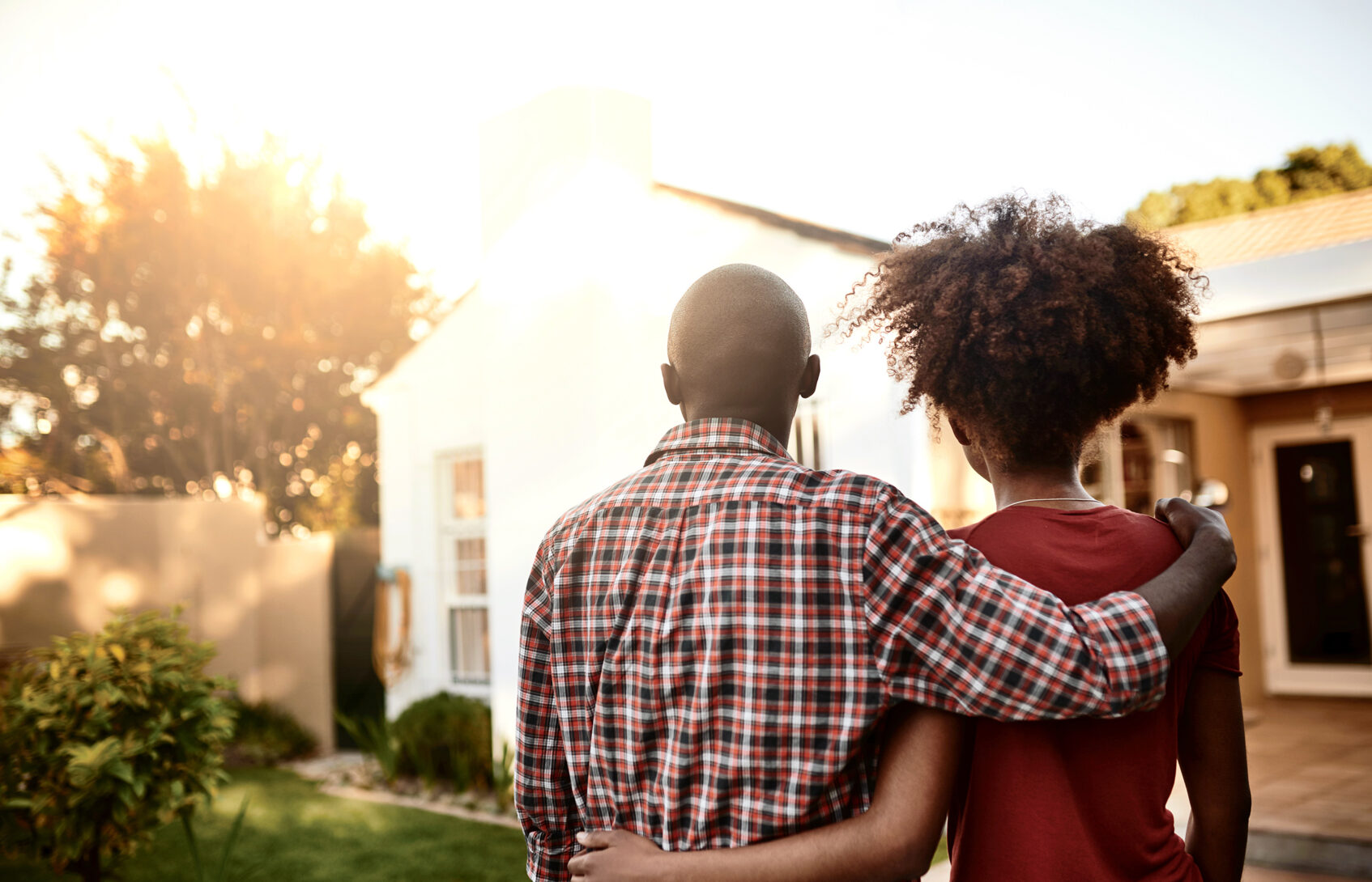 A man and a woman look at a house with their arms around each other.