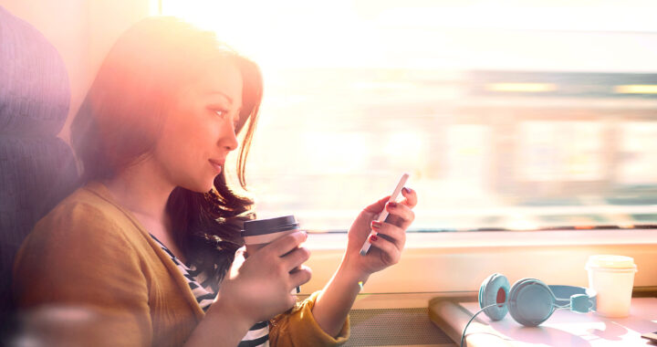 A woman looks at her phone while drinking a cup of coffee