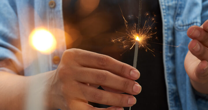 Closeup of a hand holding a burning fireworks sparkler.