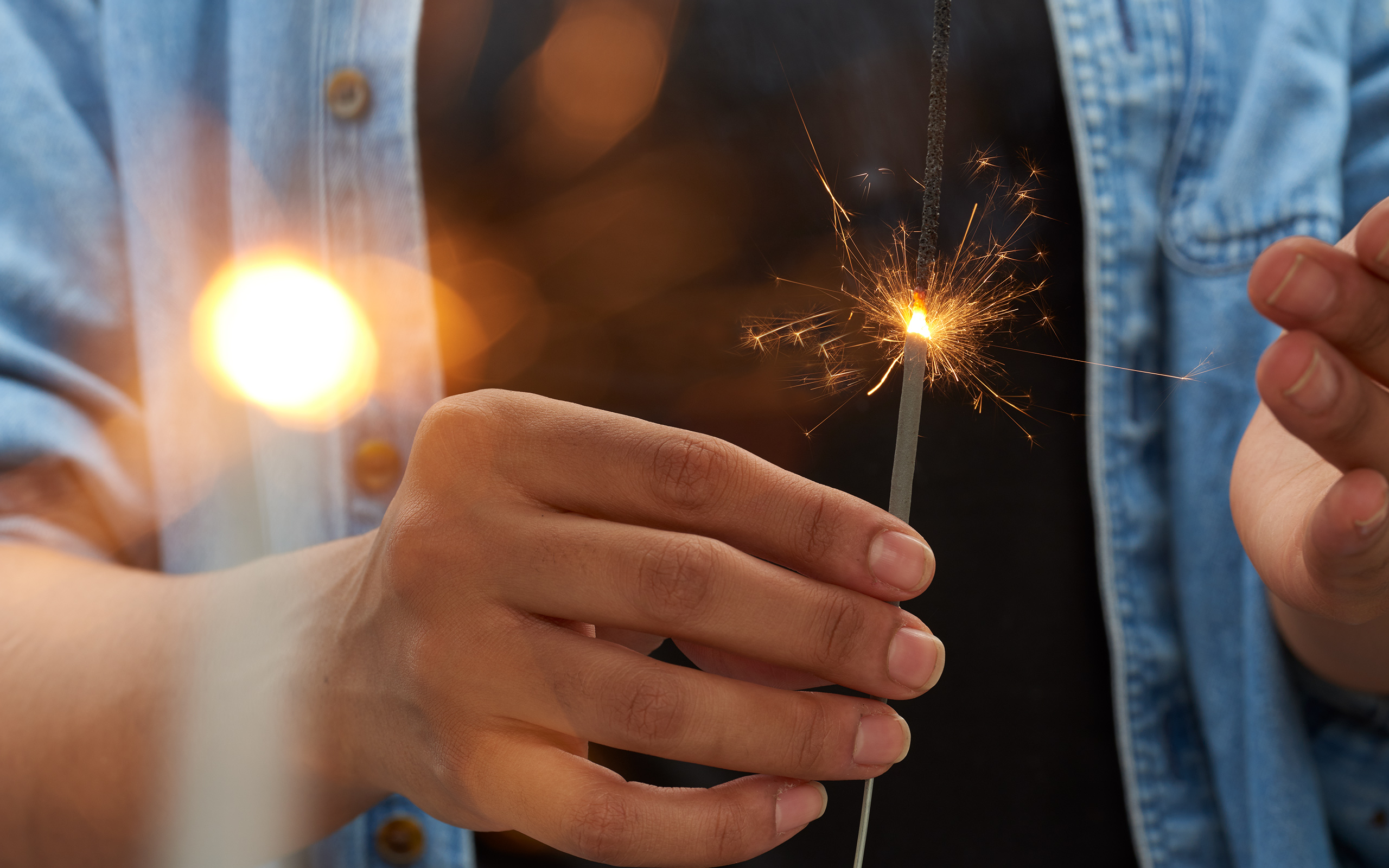 Closeup of a hand holding a burning fireworks sparkler.