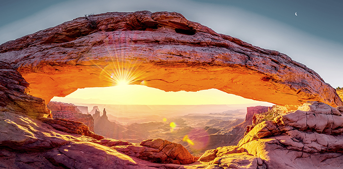 A sunset visible beneath a rock archway in Canyonlands National Park in Utah