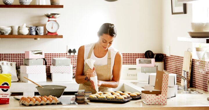 A woman wearing an apron preparing cupcakes in her kitchen.