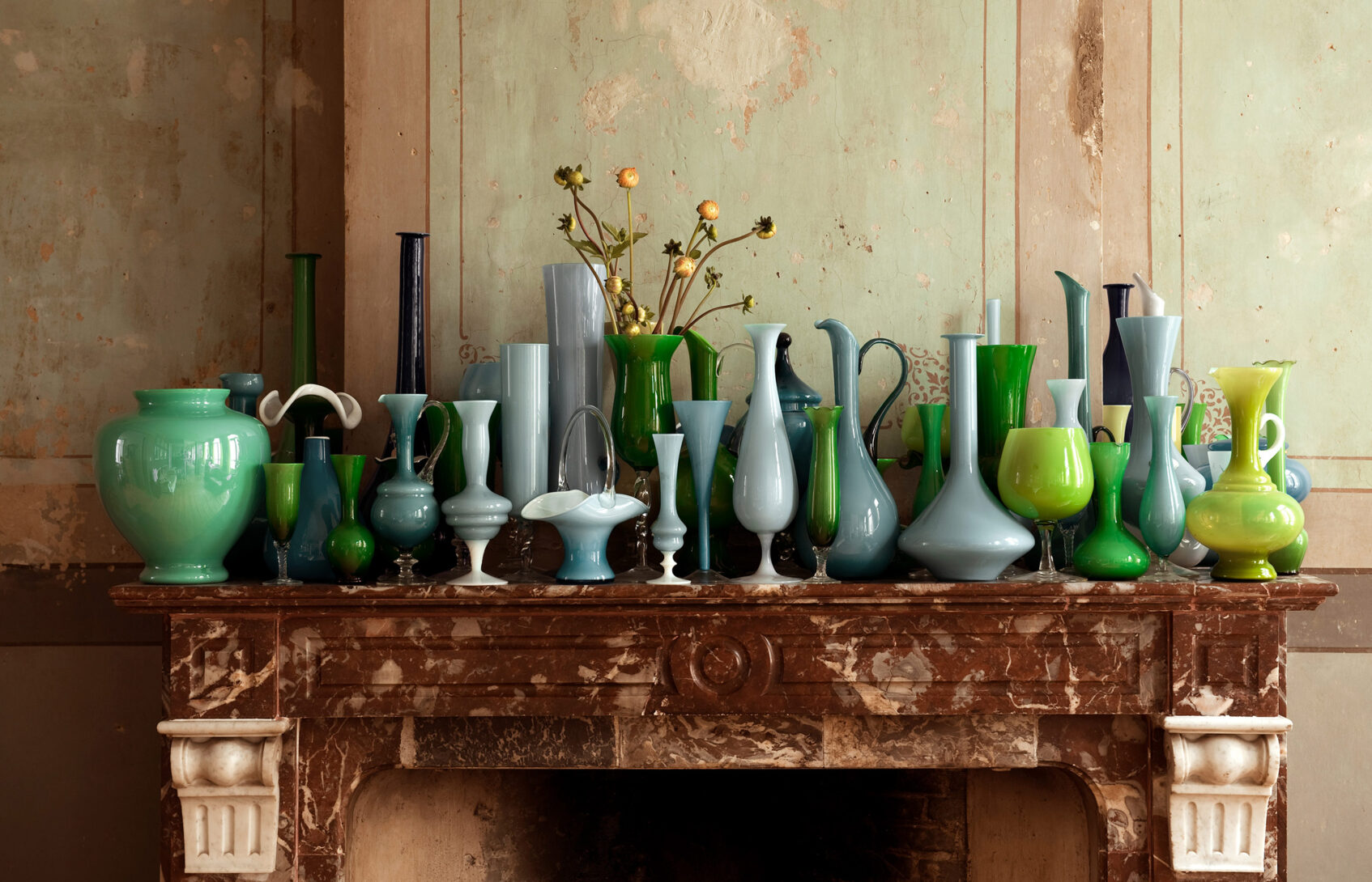 A mantle displaying an extensive collection of green and blue glass vases