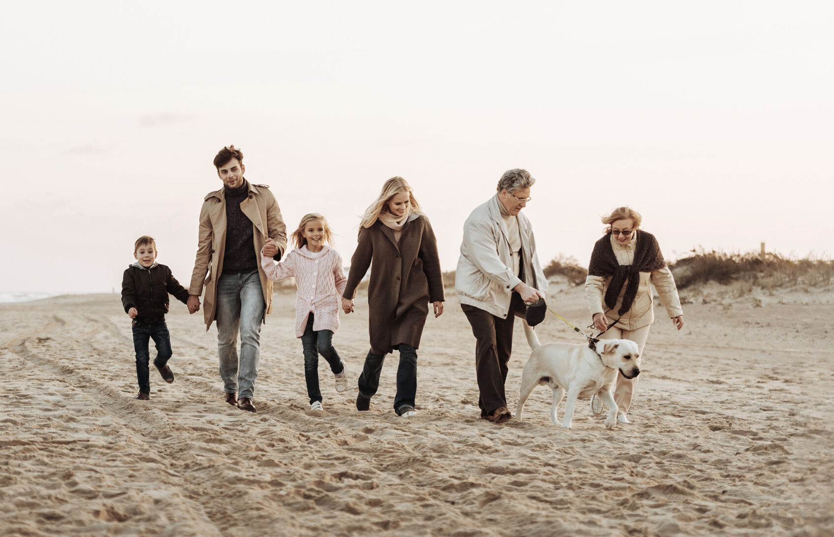 A multigenerational family walking on the beach with their dog
