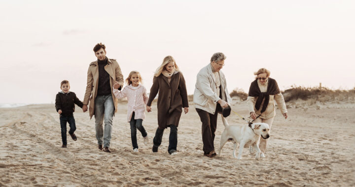 A multigenerational family walking on the beach with their dog