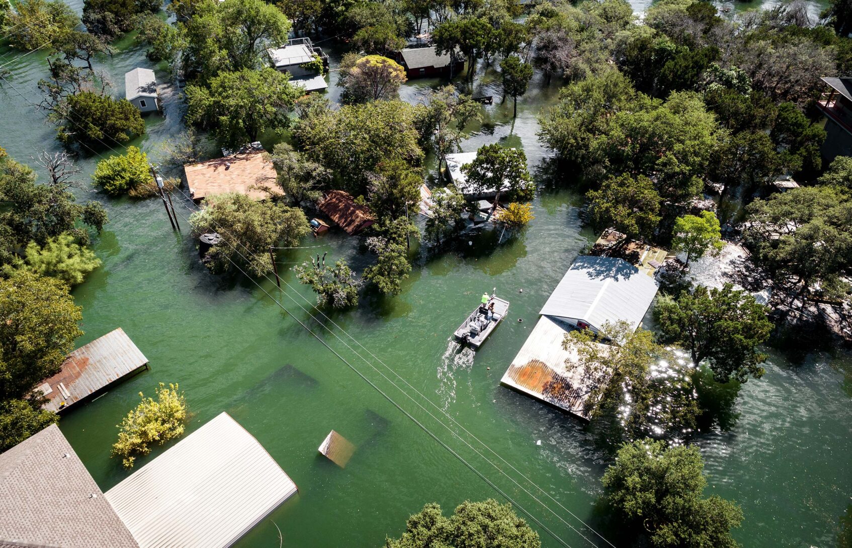 An aerial view of roofs and trees in a flooded neighborhood