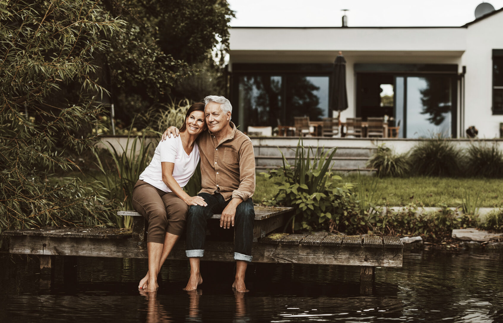 Smiling senior man sitting with arm around woman on jetty by lake