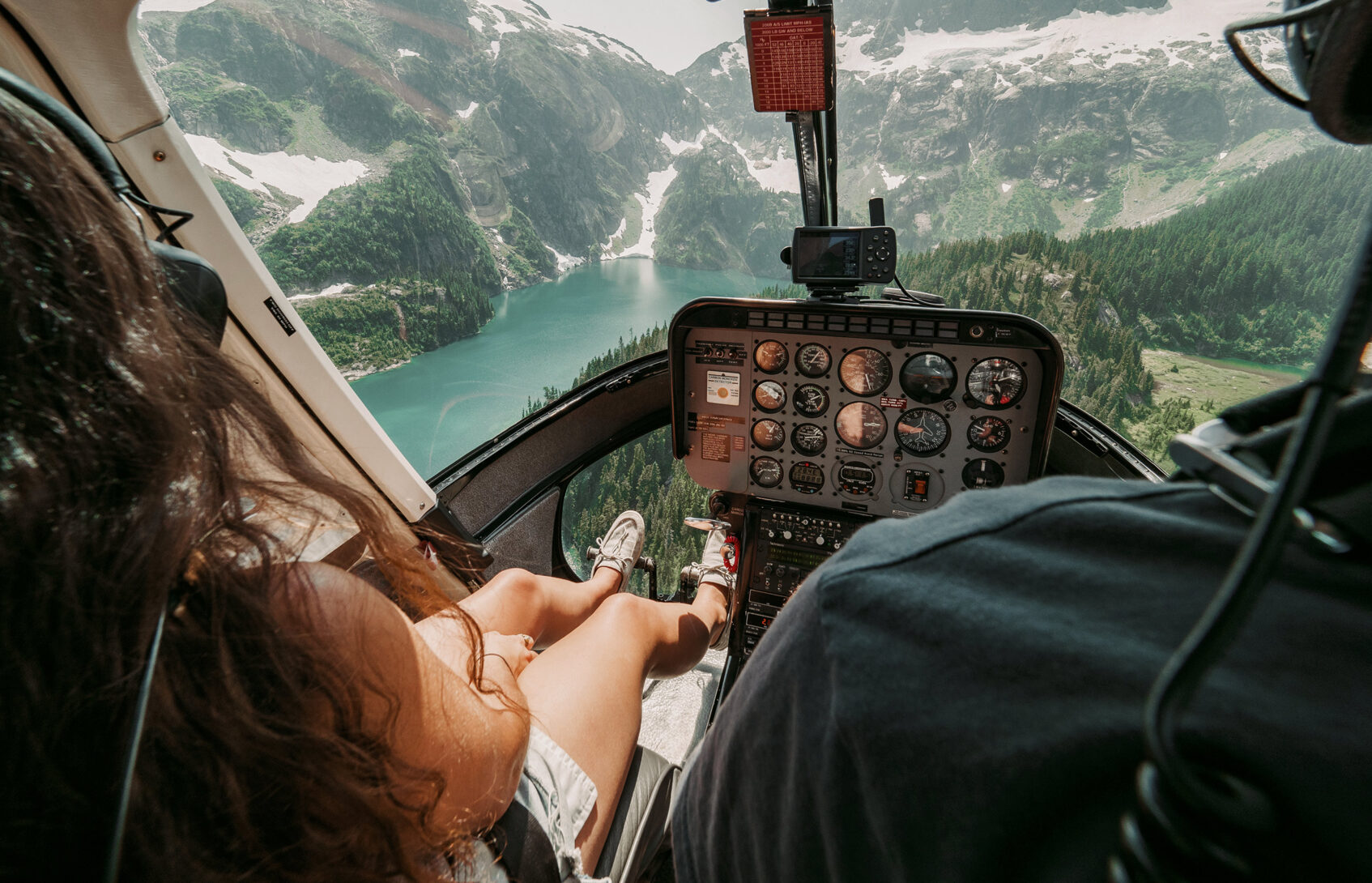 A person traveling in the cockpit of a helicopter sees mountains, waterfalls, and a lake below