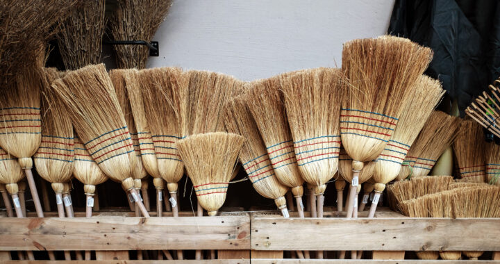 A collection of corn straw brooms stand together in a bin.
