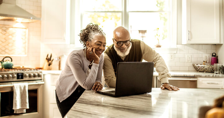 A senior couple looking at a laptop in the kitchen.