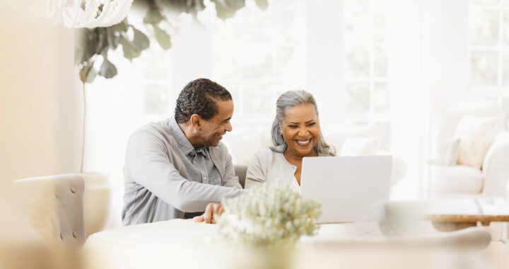 A husband and wife looking at a computer screen and smiling.