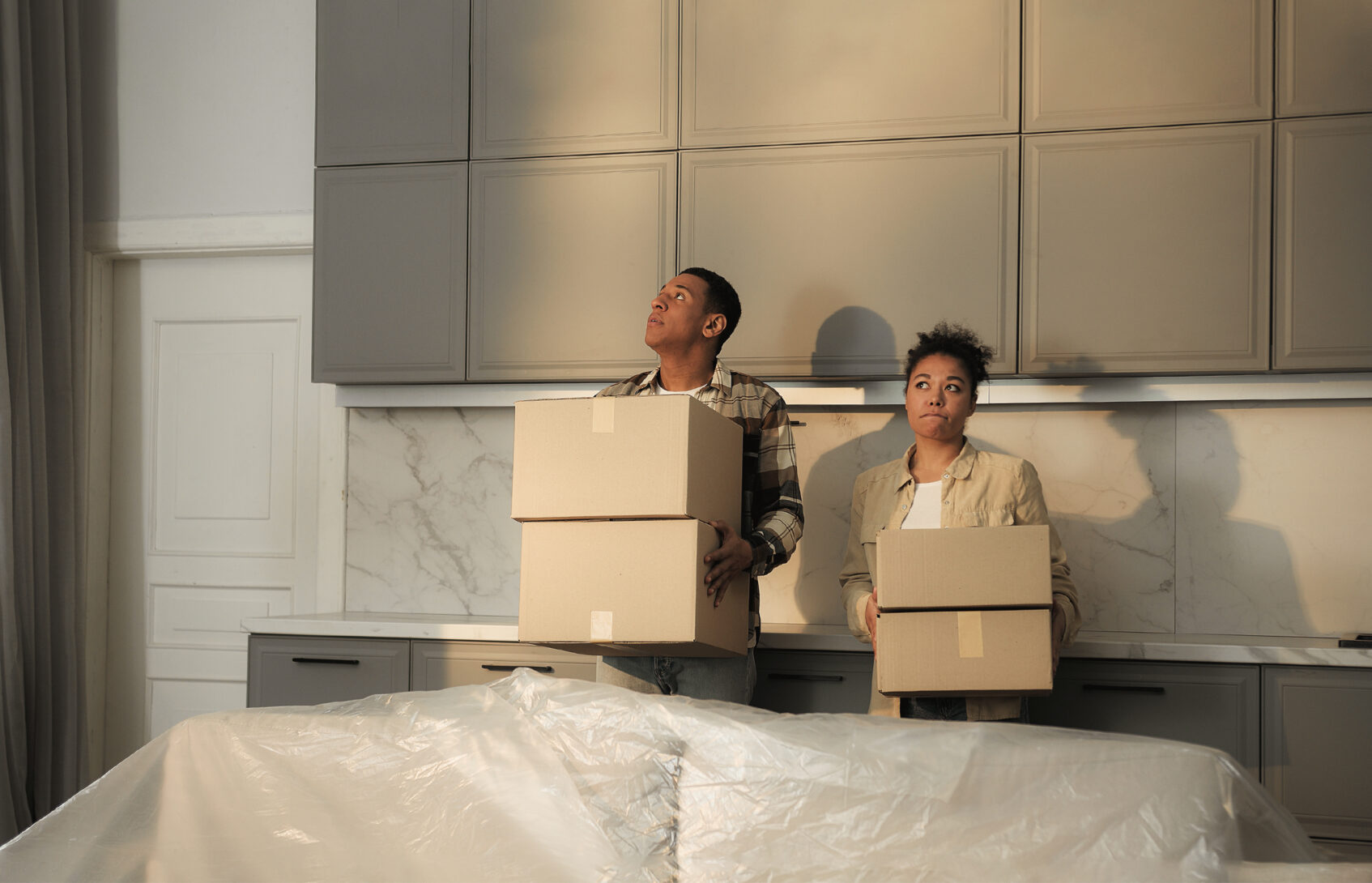 A contemplative married couple is holding moving boxes in their kitchen.