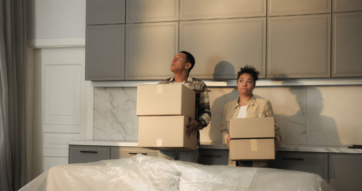 A contemplative married couple is holding moving boxes in their kitchen.