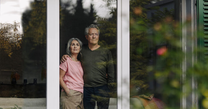 Senior couple behind windowpane of their home