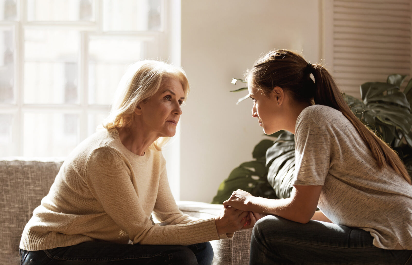 A mother and daughter seated across from each other and holding hands.