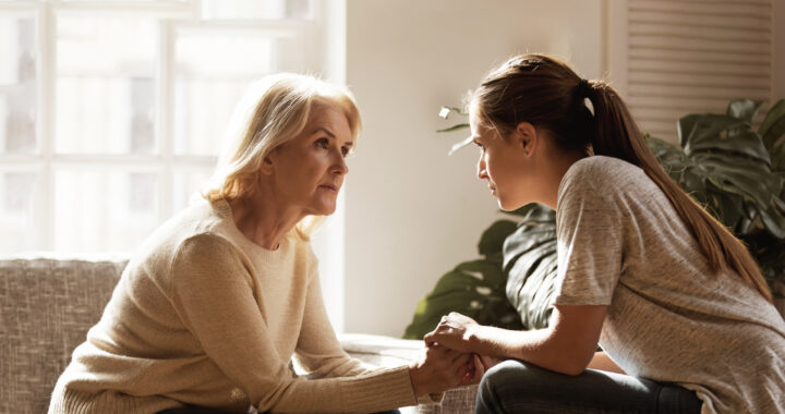 A mother and daughter seated across from each other and holding hands.