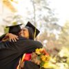 Two students hug while wearing graduation caps and gowns.