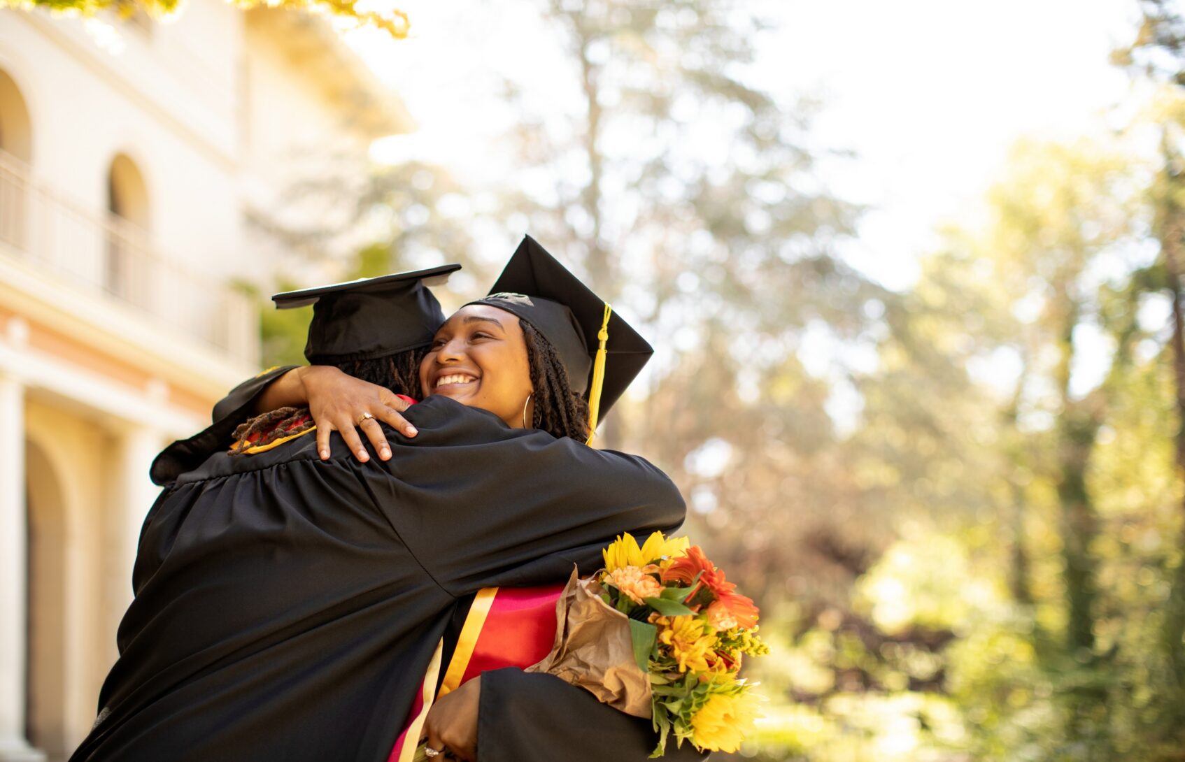 Two students hug while wearing graduation caps and gowns.