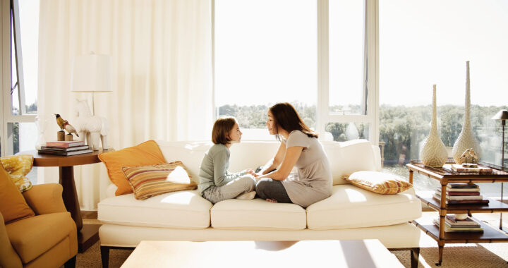 A mother and daughter seated on a couch talking to each other.