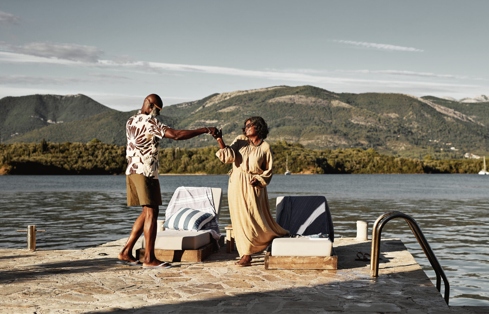 A happy married couple dancing on a stone pier beside a lake.