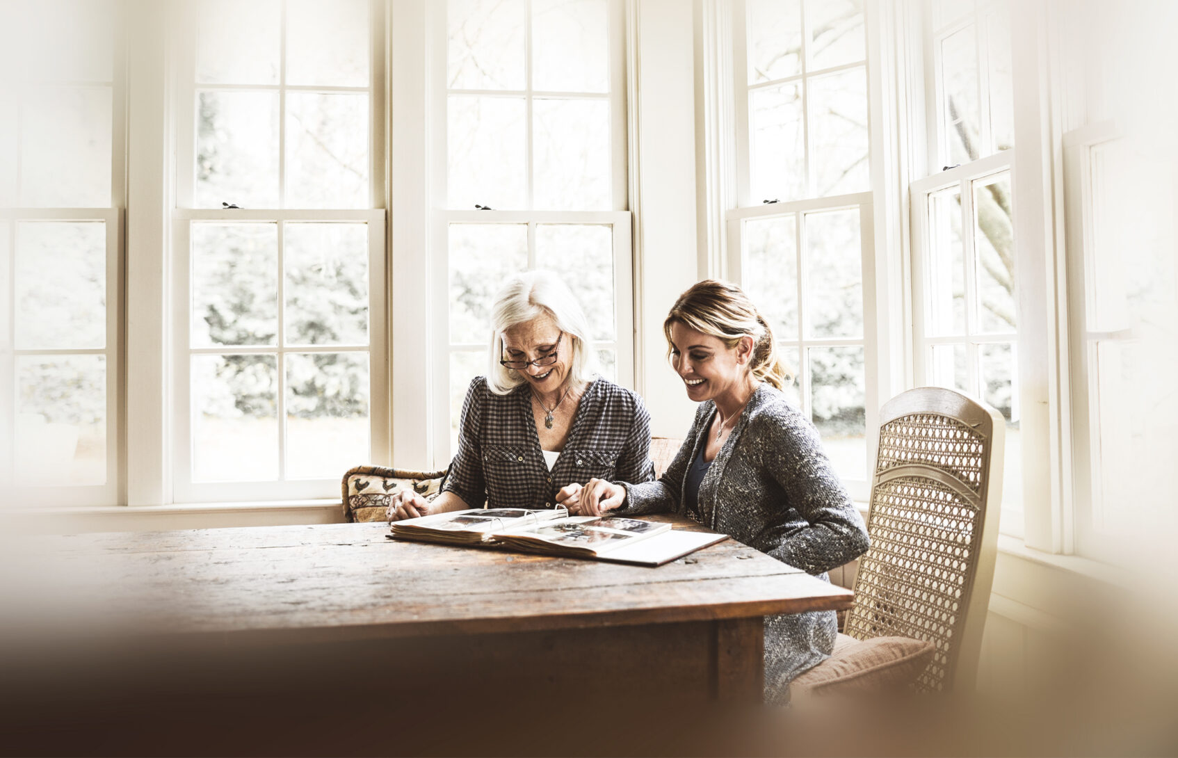 A mother and daughter seated at a table looking at a photo album.