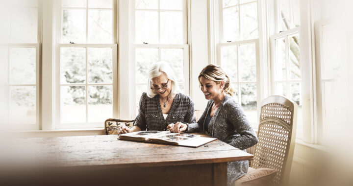 A mother and daughter seated at a table looking at a photo album.