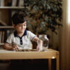 A child sits at a table, organizing coins into a jar for his savings Read about Tips for raising financially savvy children