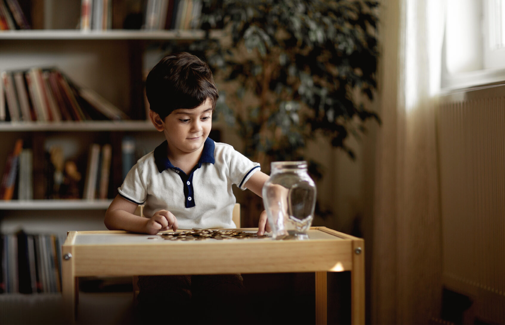 A child sits at a table, organizing coins into a jar for his savings