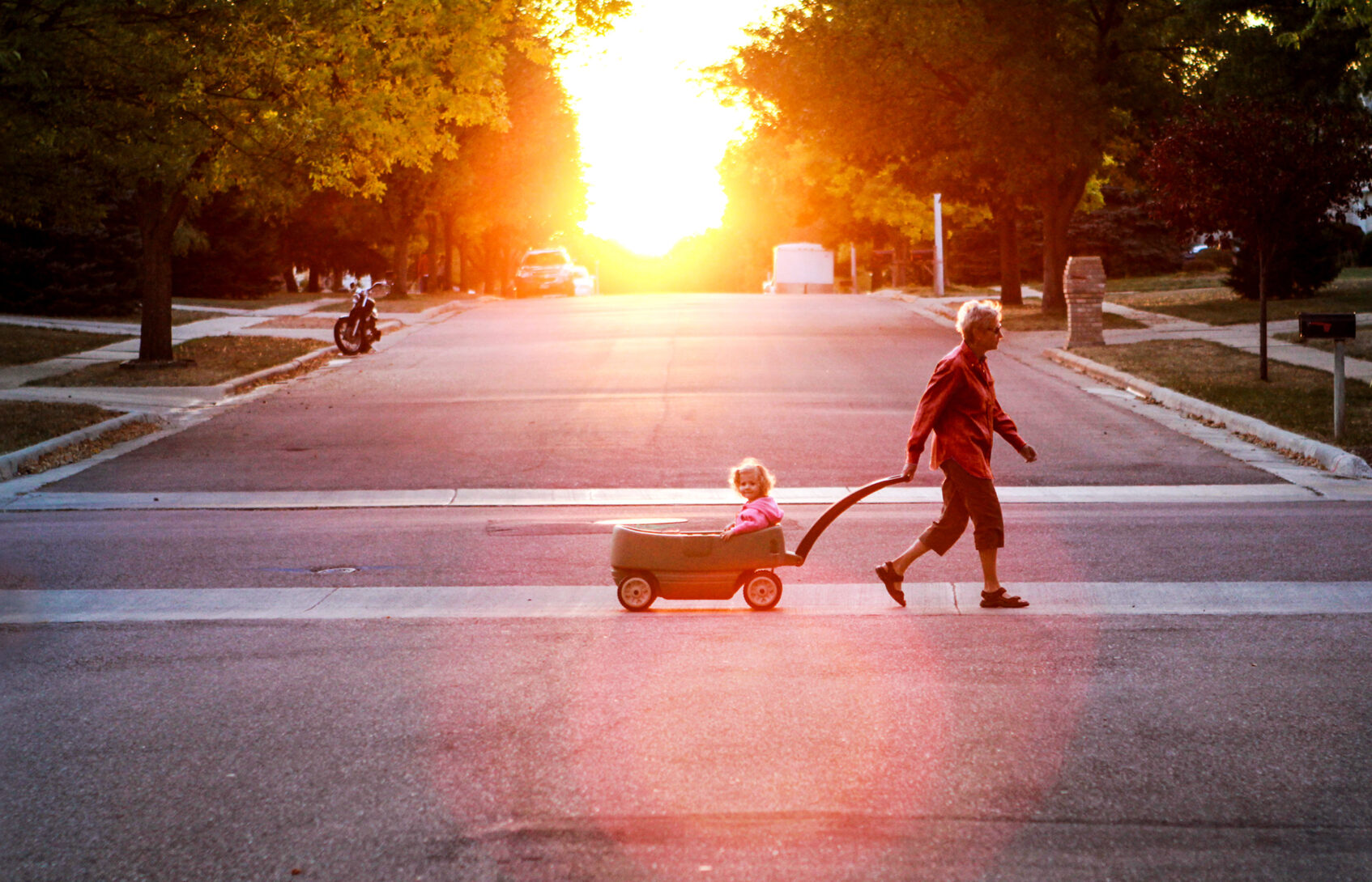 A grandparent pulls a young child in a wagon across the street