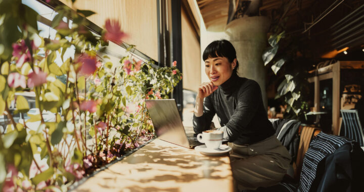A woman sits in a café, working from her laptop computer.