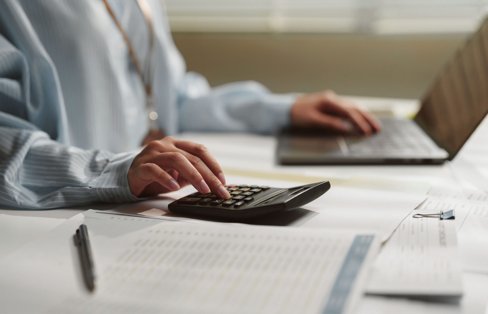 Female accountant using a calculator while working on financial documents and a laptop.