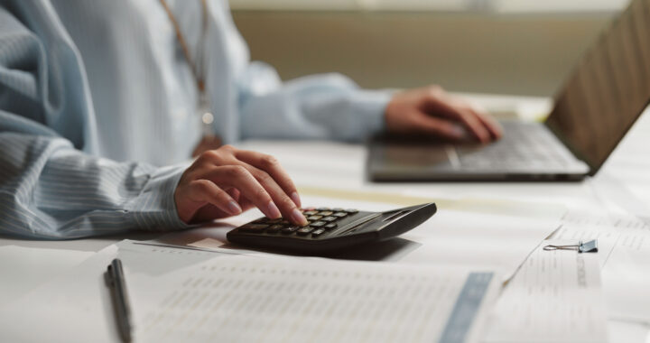 Female accountant using a calculator while working on financial documents and a laptop.